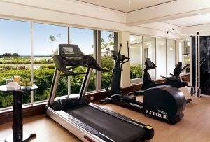 fitness center und sport bereich mit glaswand und ausblick auf den dschungel die palmen und das meer neben den fitness geräten steht ein hoher tisch mit handtüchern säften und früchten im edlen exotischen luxuriösen und hochklassigen disgner hotel resort 